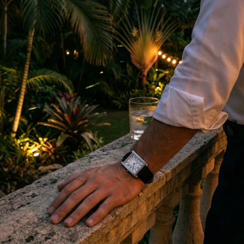 Pulso masculino com relógio Fabbricantti caixa retangular aço pulseira couro preto apoiado em mureta de pedra jardim tropical noturno lifestyle luxo ao ar livre